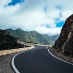 Jalan berkelok melewati pegunungan hijau yang menggambarkan konsep perjalanan panjang